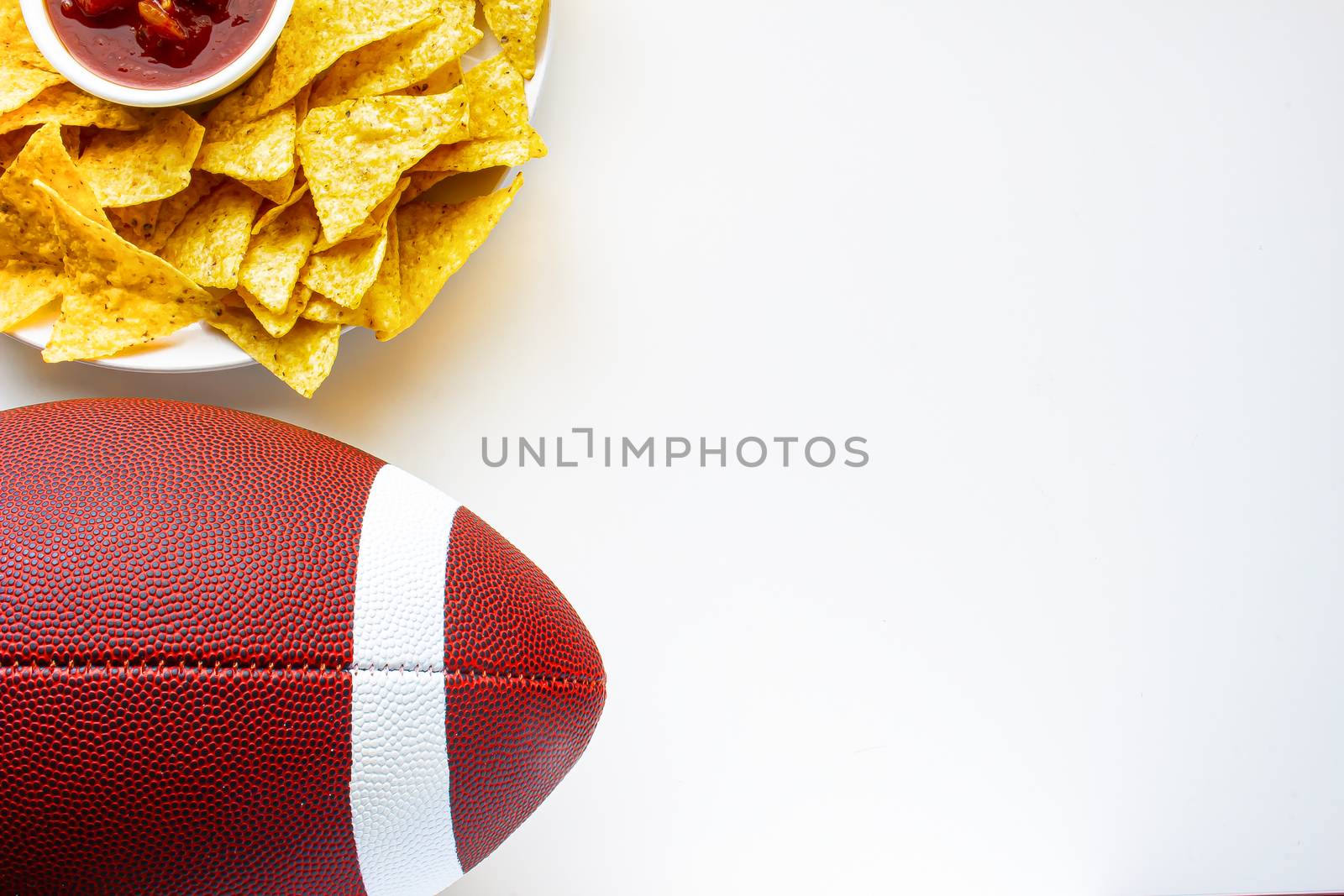 An American football with organic nacho chips and mild salsa on the side on a white background