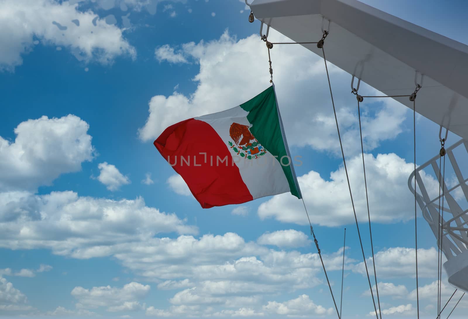 A Mexican flag flying under cloudy skies on a white cruise ship