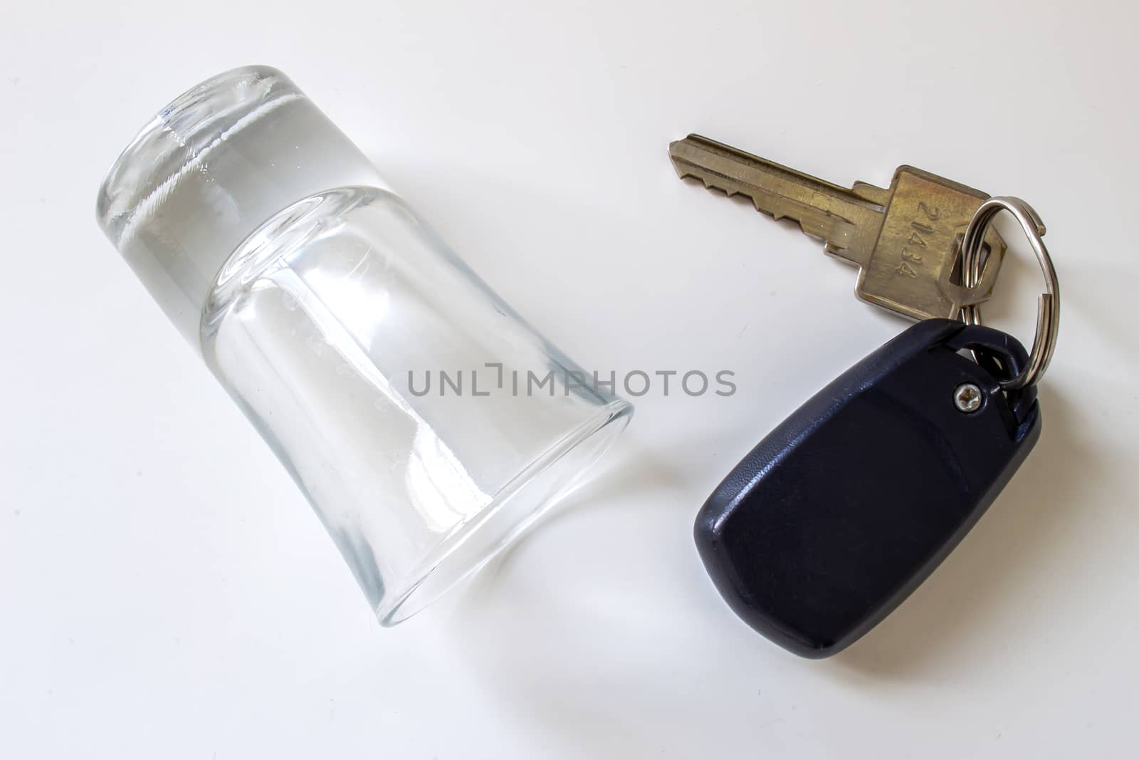 Don't drink and drive. An empty shot glass on a white background with car keys