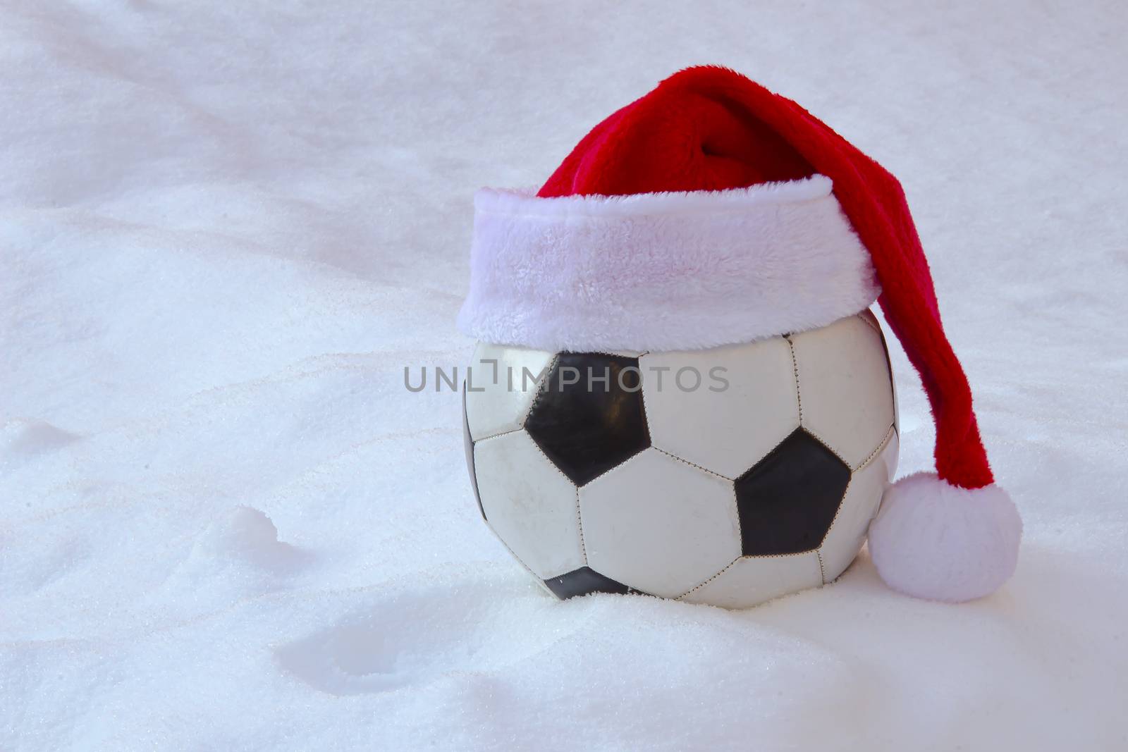 Soccer ball with a Santa hat on snow for Christmas