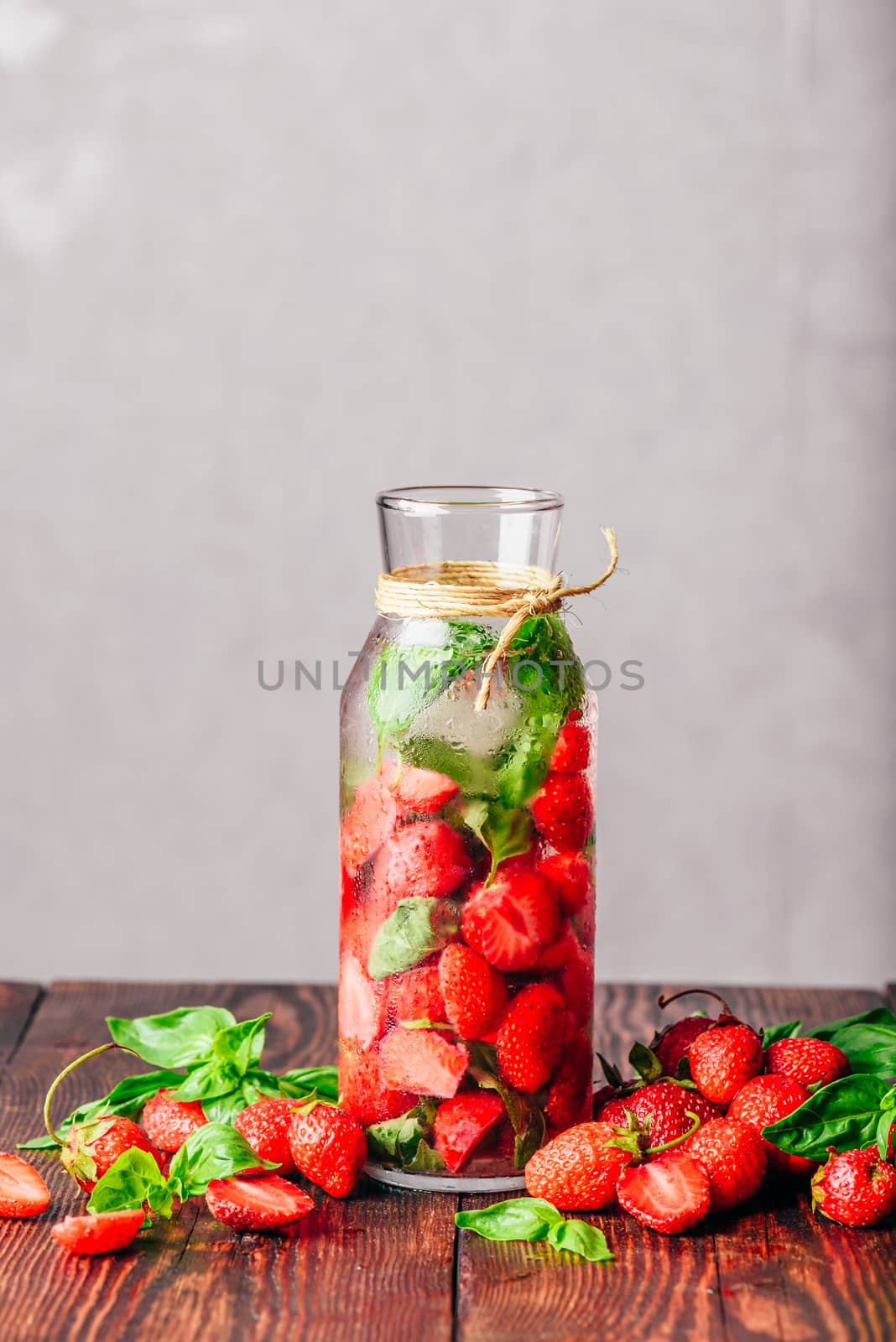 Bottle of Water Infused with Fresh Strawberry and Basil Leaves. Scattered Ingredients on Wooden Table. Vertical Orientation and Copy Space.