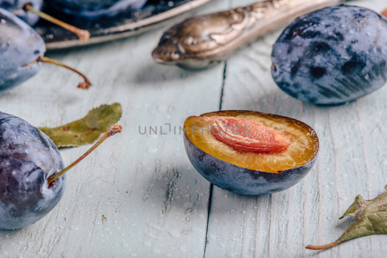 Ripe plums with sliced fruits, leaves and vintage knife over light wooden surface