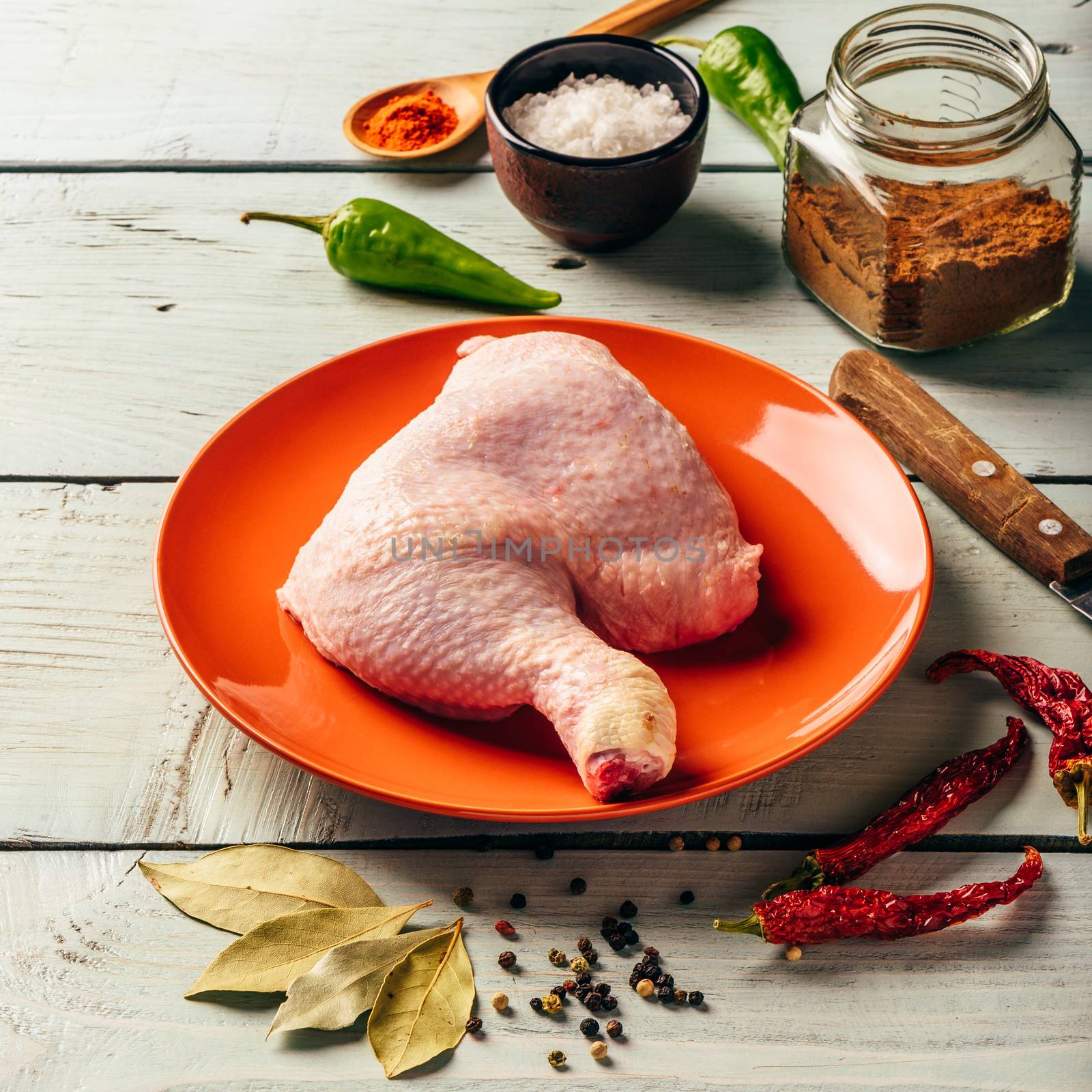 Chicken leg quarter on orange plate over wooden surface with different spices