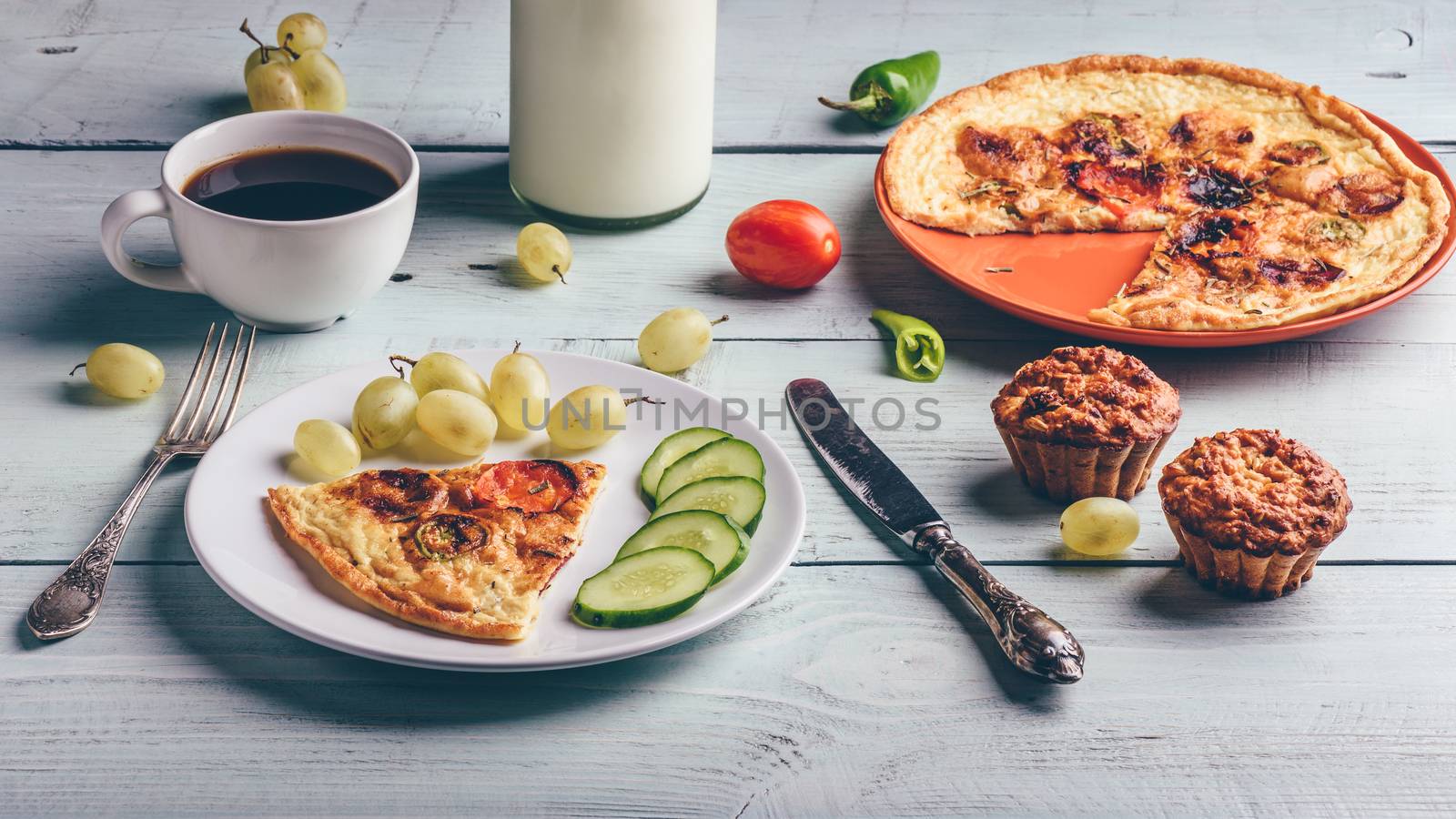 Healthy breakfast with frittata, fruits, vegetables, milk, cup of coffee and muffins on light wooden background.