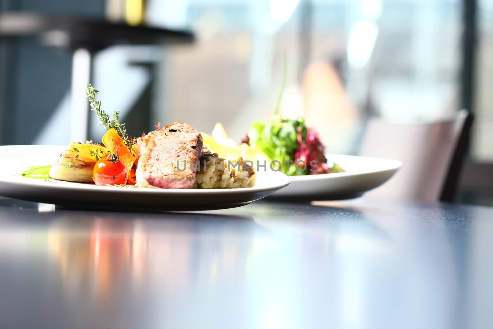 a good meal with meat and salad on white plates with restaurant setting. Table and window in the background