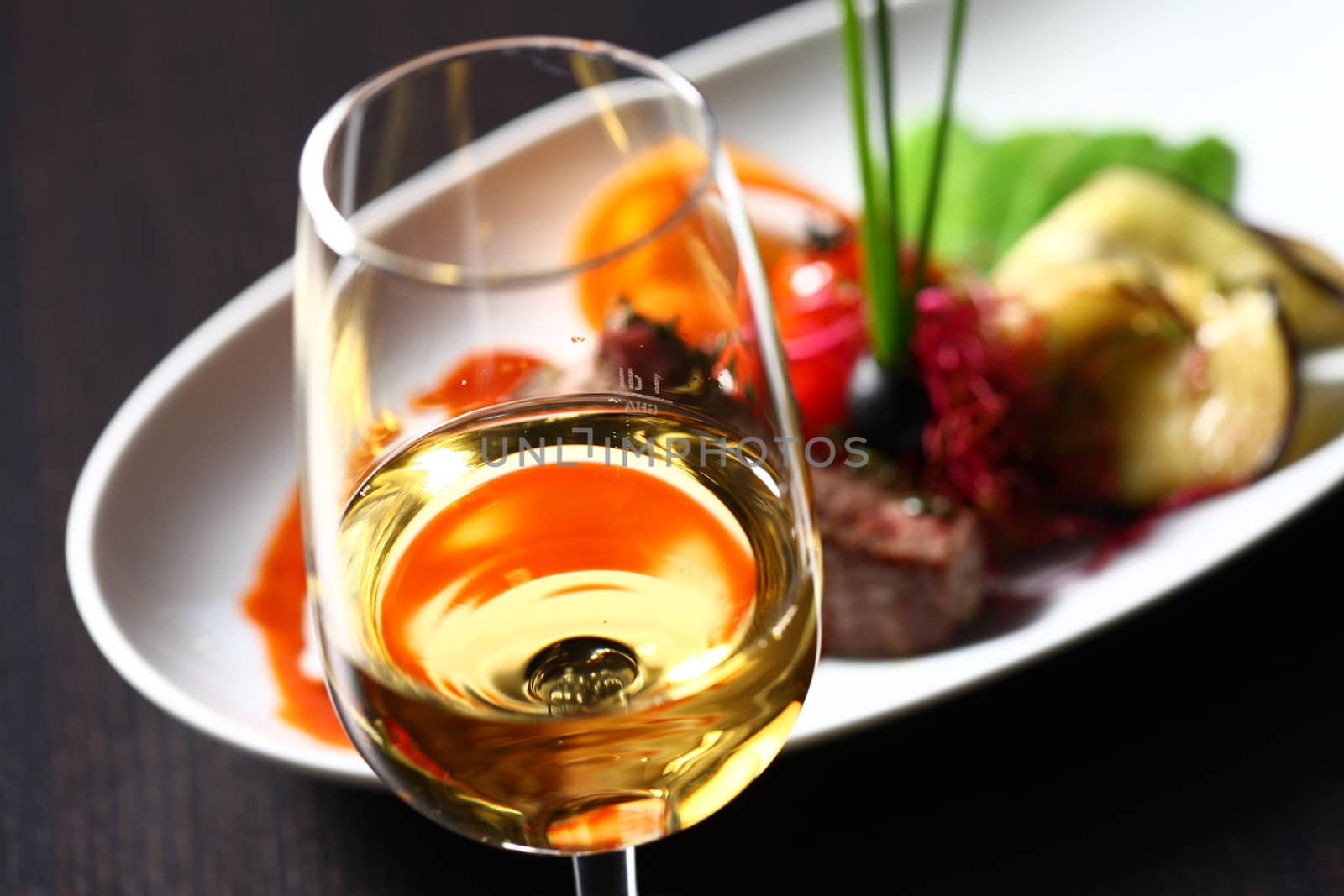 a good meal with wine. Close up of out of focus wine glass with dish in the background showing through the glass on a dark background