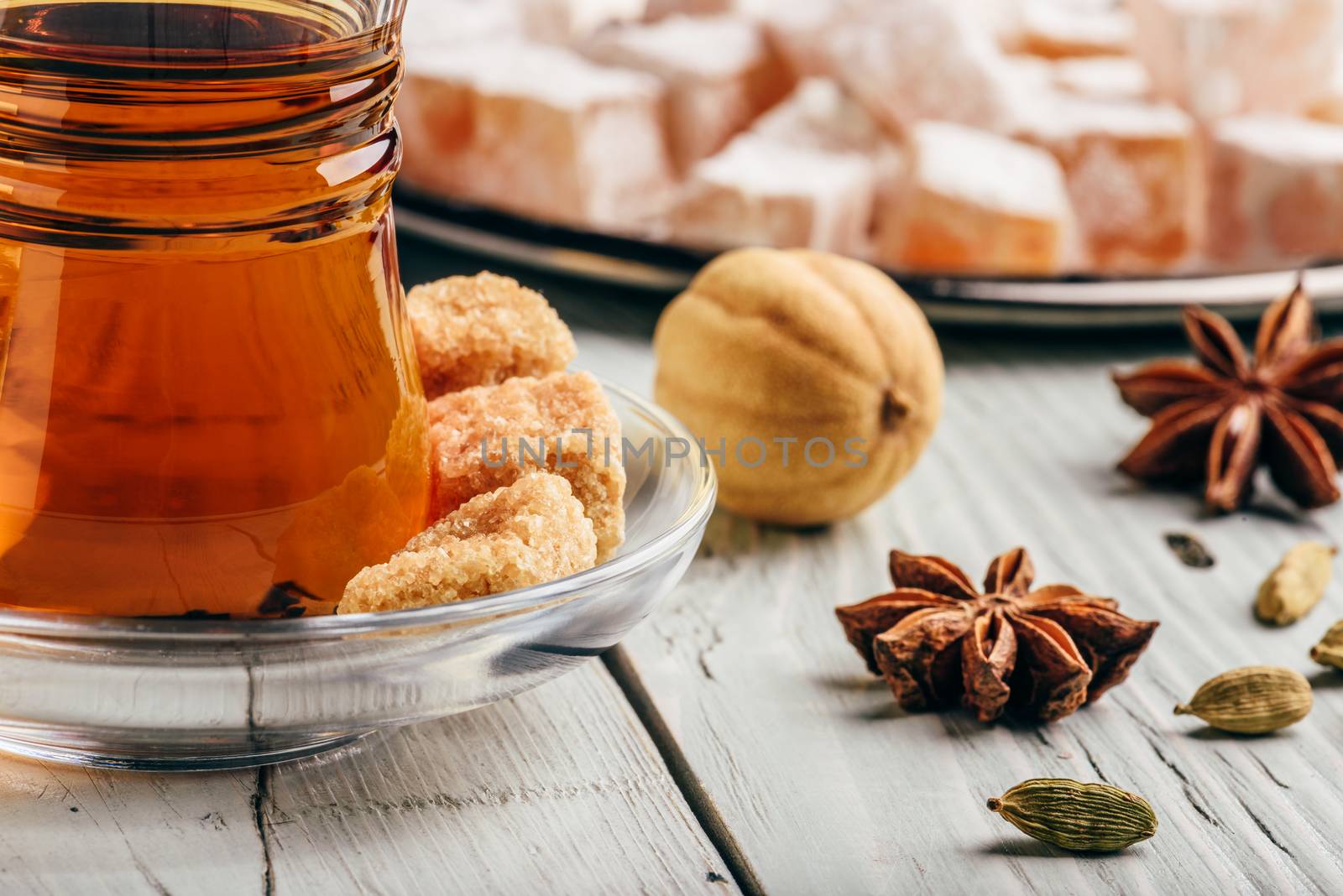 Tea in arab glass with turkish delight Rahat Lokum and different spices over wooden surface