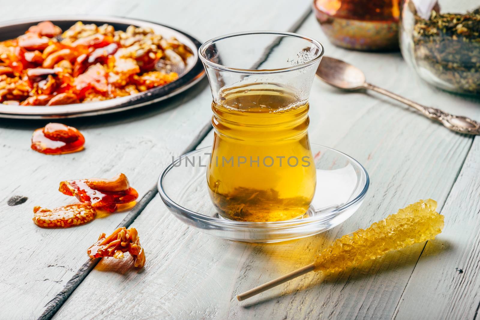 Herbal tea in oriental glass with arabian nut delights on metal plate over light wooden surface