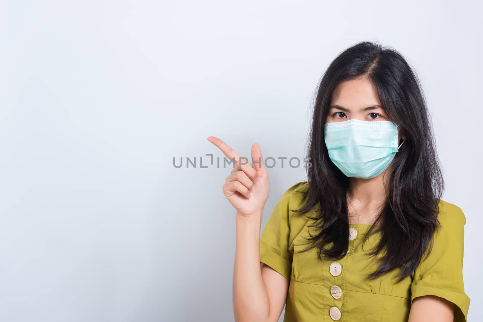 Portrait Asian beautiful happy young woman wearing face mask protects filter dust pm2.5 anti-pollution, anti-smog, and air pollution her pointing out to space on a white background, with copyspace