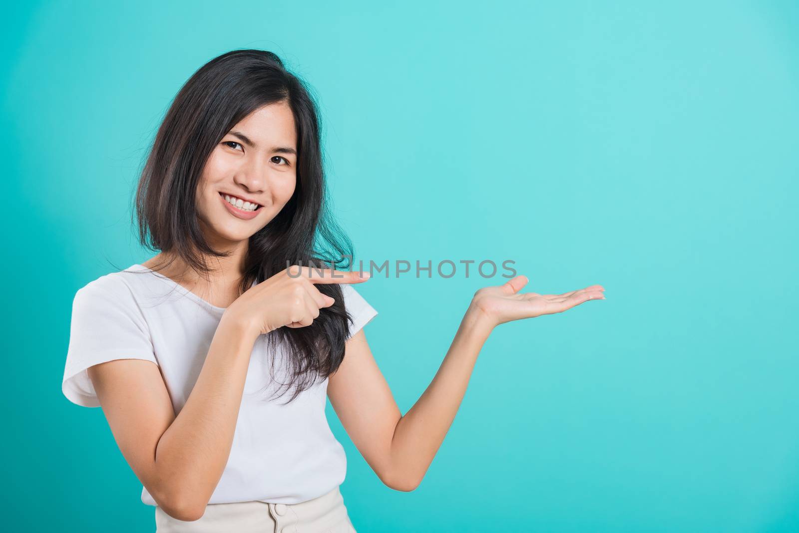 Portrait Asian beautiful young woman standing wear t-shirt, She showing hand to presenting product and looking at the camera, shoot photo in a studio on blue background, There was copy space
