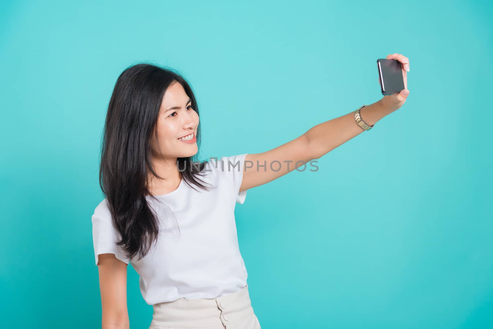 Portrait Asian beautiful happy young woman standing smile, holding mobile phone her taking selfie on blue background, with copy space