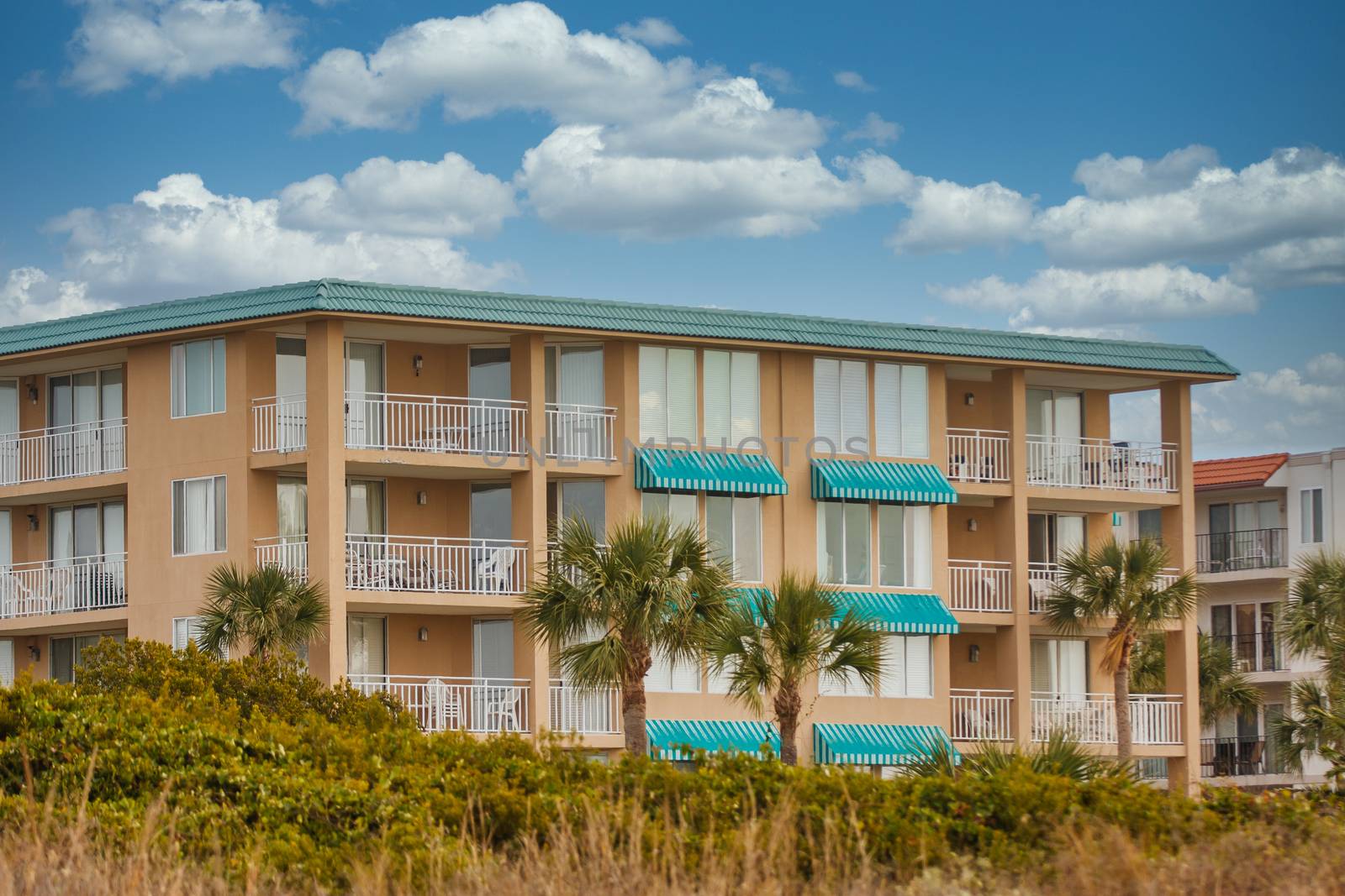 A coastal condo building of pink stucco with green metal roof and awnings