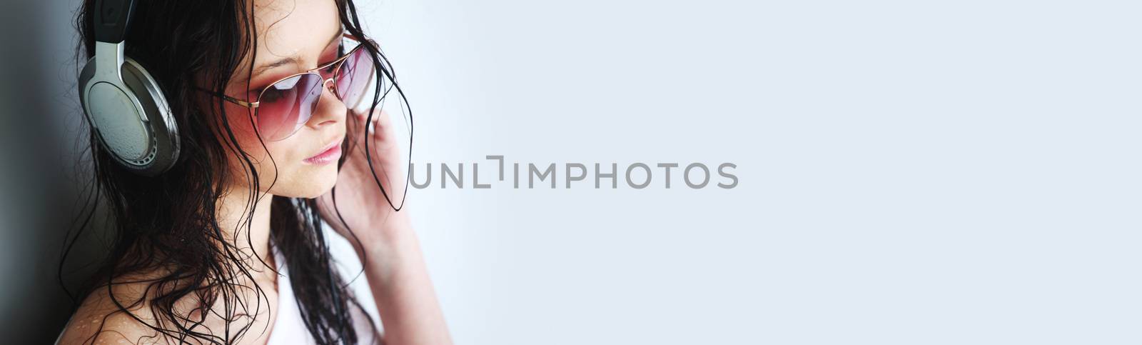 Young woman listening to music on headphones enjoying a dance. Closeup portrait of girl on light background with copy space