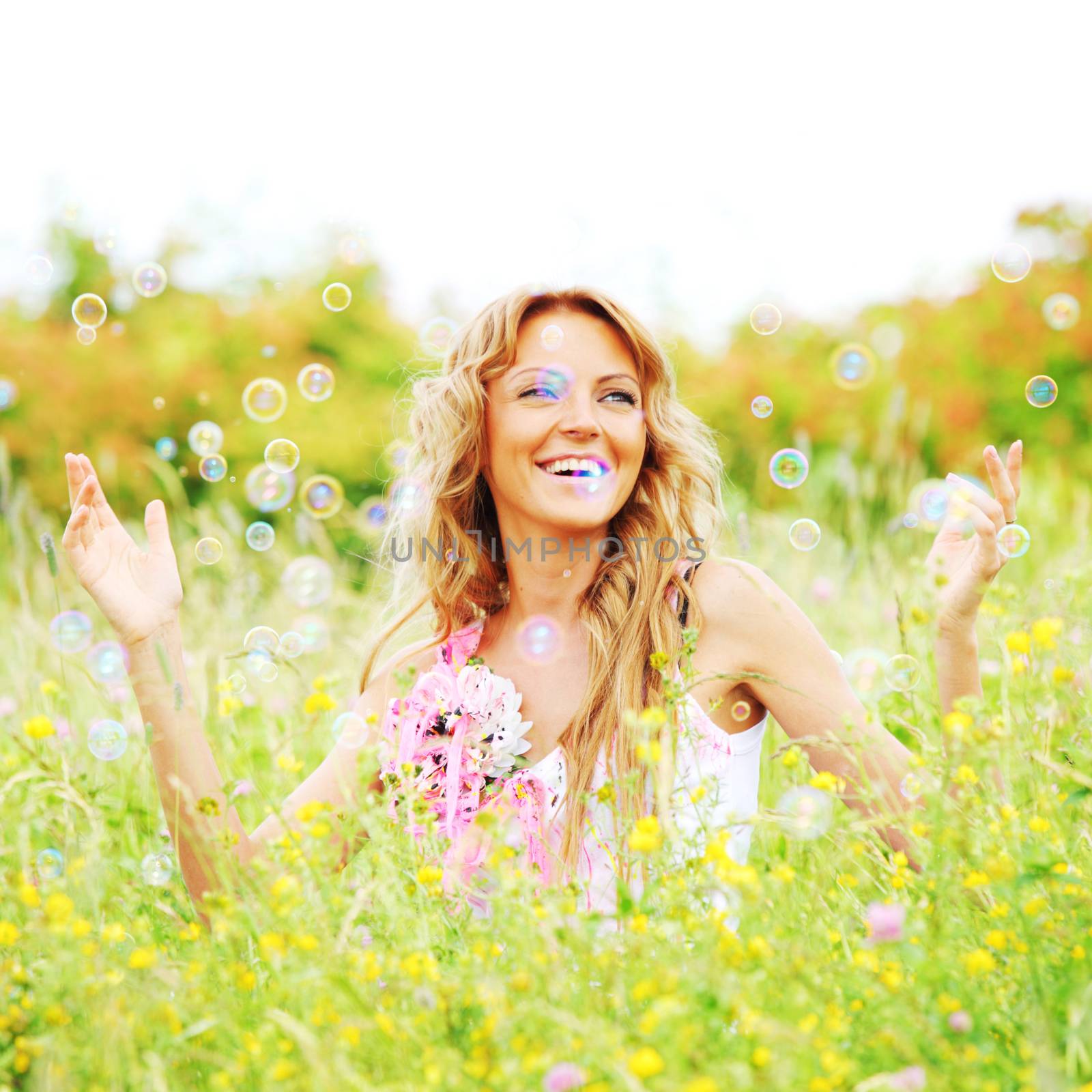 Blonde girl starts soap bubbles and smiling in a green spring field