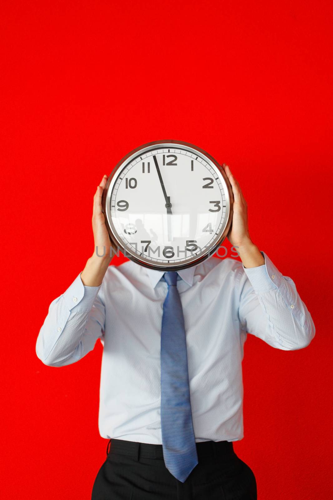 Businessman covering his face with wall clock on red background