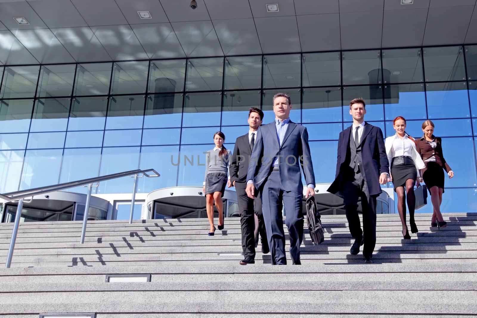 Group of business people and their leader walking down stairs outside office building successul deal negotiation concept
