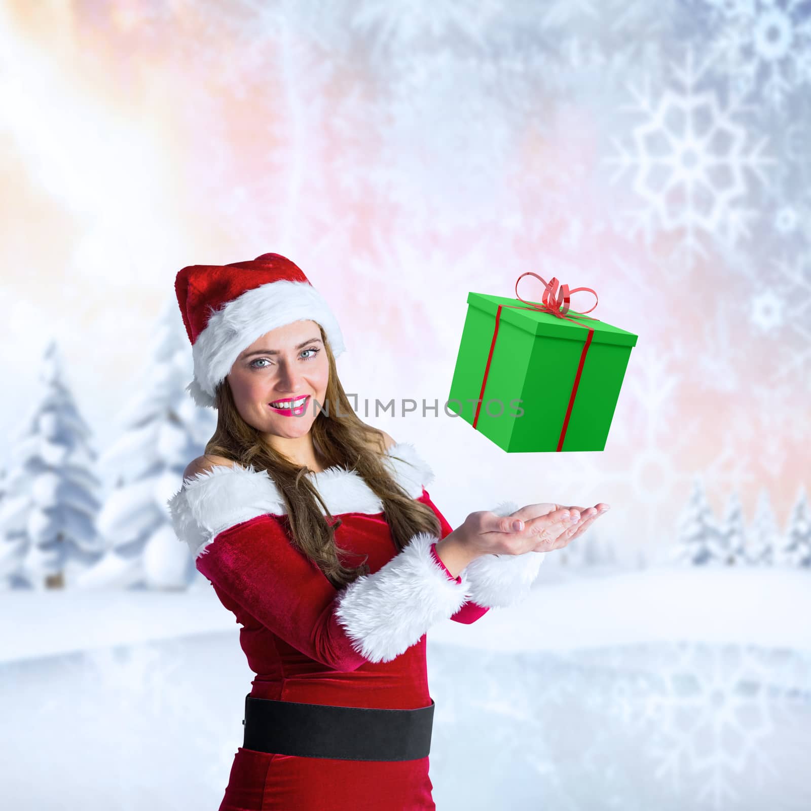 Pretty girl in santa costume holding hand out against snowy landscape with fir trees