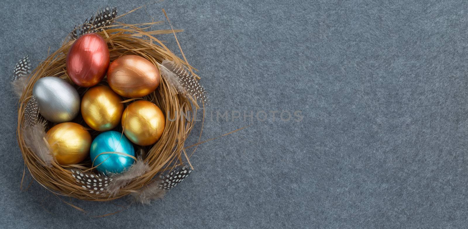 Happy Easter holiday greeting symbol stylish natural wooden grass nest with colorful quail eggs and feathers on gray fabric background with copy space for text