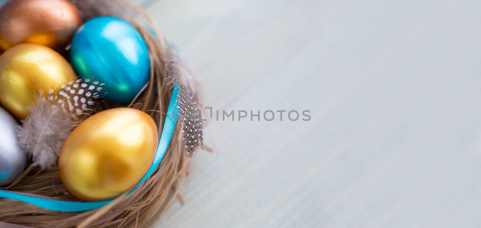 Beautiful Happy Easter holiday greeting banner with easter nest with colored eggs and decorated with ribbons and feathers over light wooden background with copy space for text