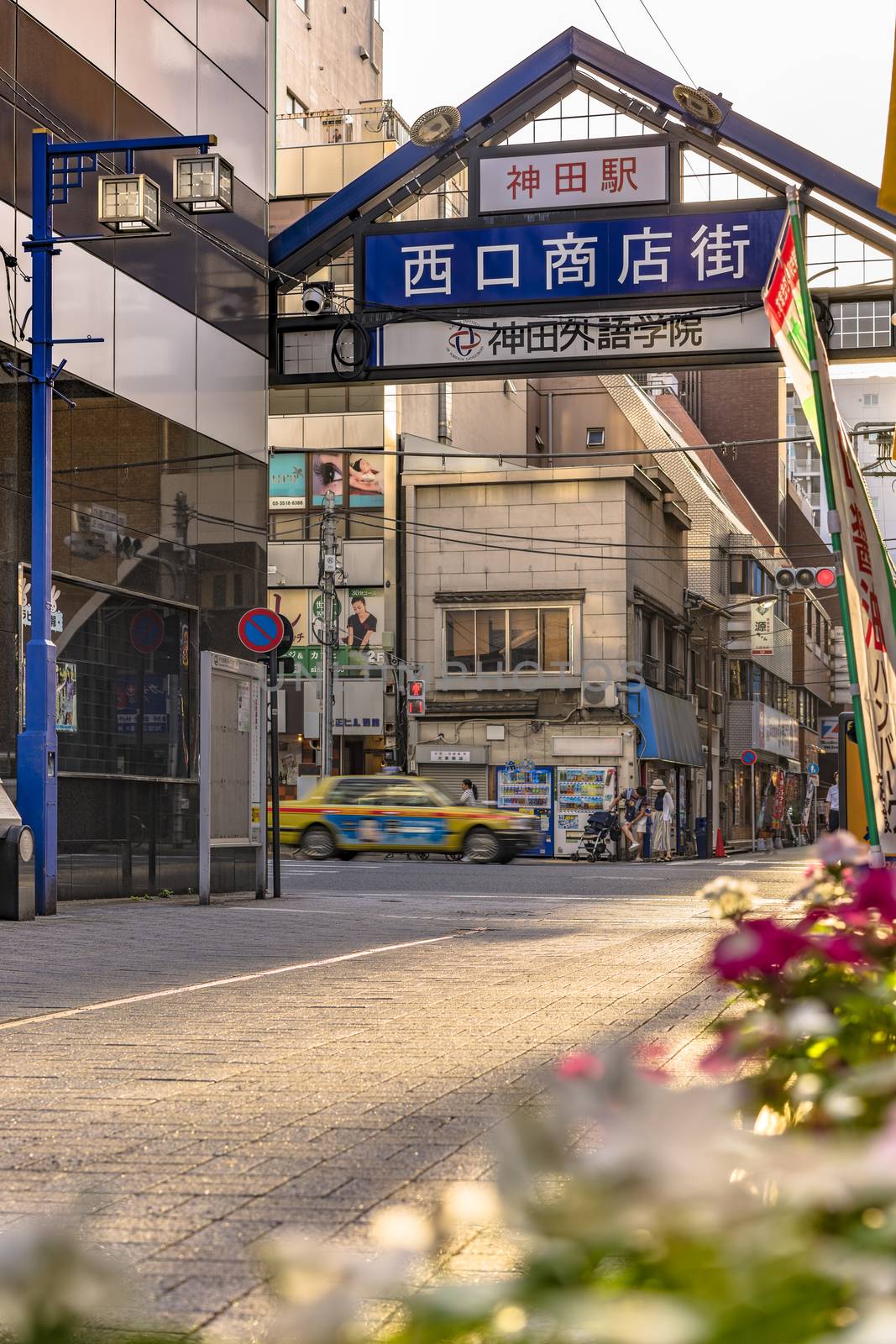 Blue metal entrance gate of the shopping street decorated with flowers from the west exit of Kanda Station on the Yamanote Line. The street extends over 300 meters and has no less than 100 shops.