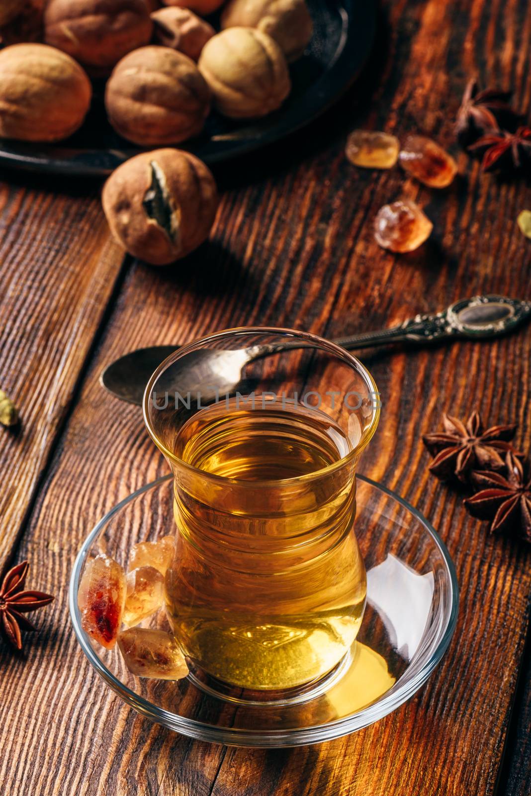 Spiced tea with star anise, cardamom and dried lime in oriental glass over wooden surface