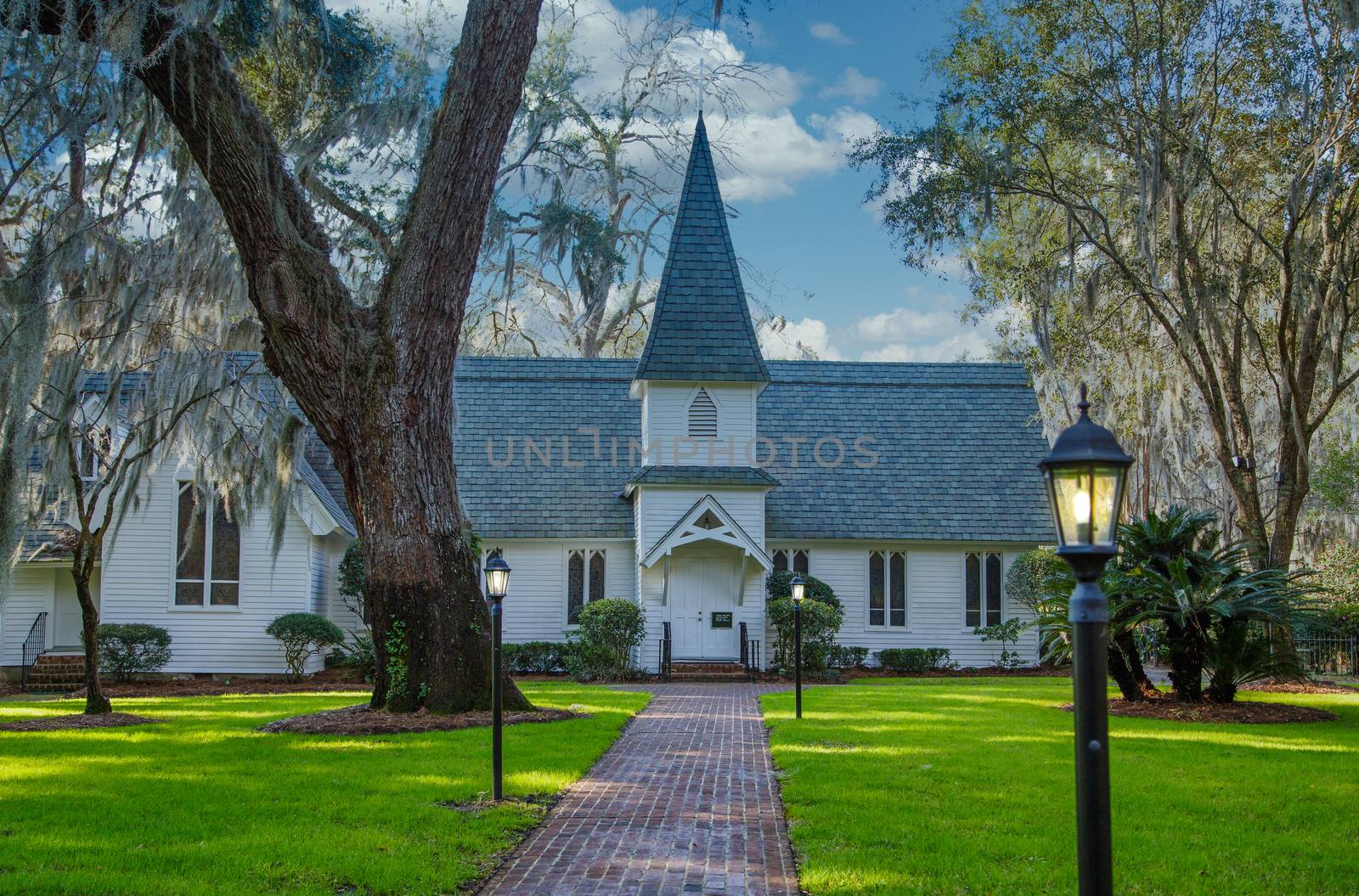 Small Church Past Brick Walk and Green Lawn with Lamps by dbvirago