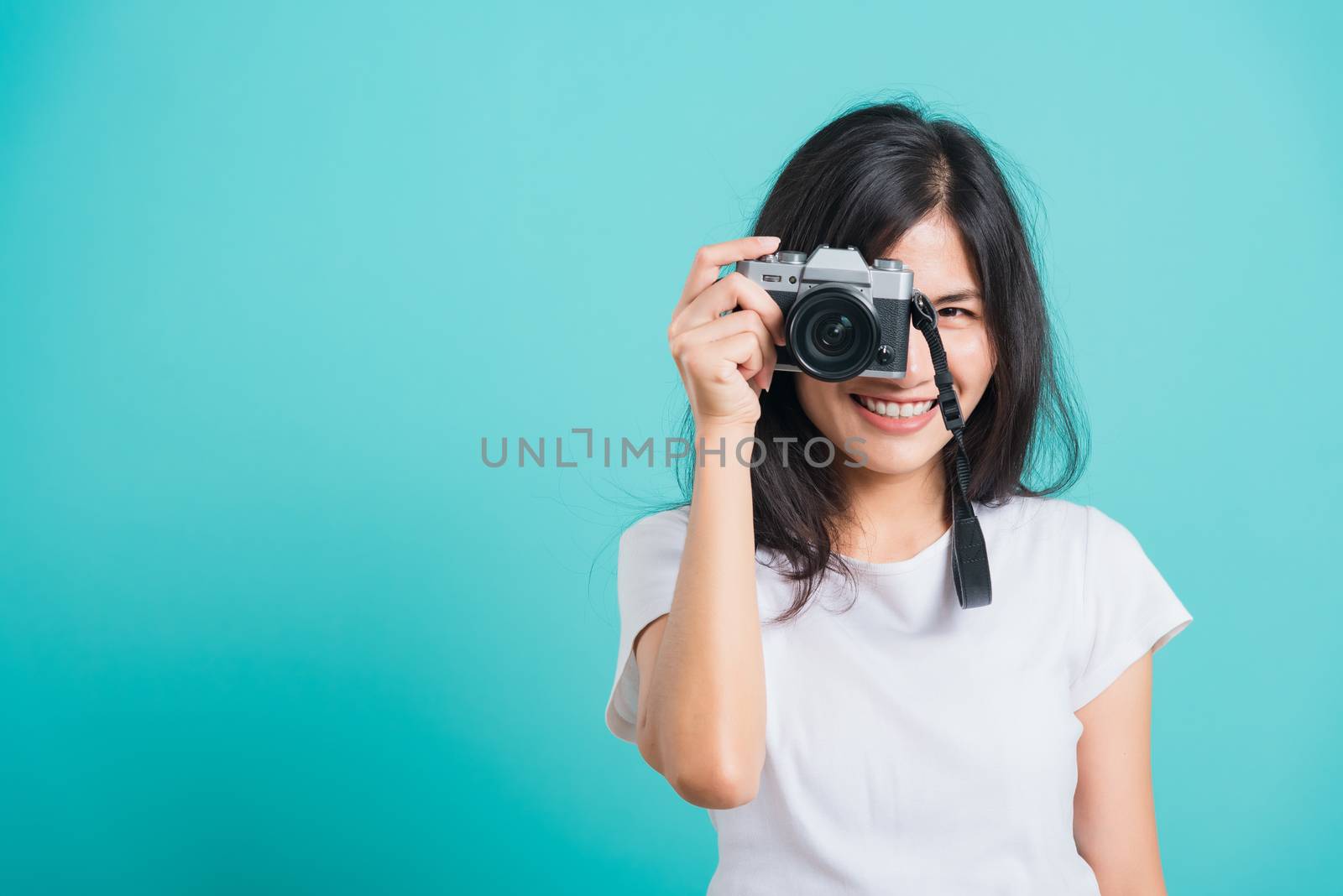 Traveler tourist happy Asian beautiful young woman smile in summer hat standing with mirrorless photo camera, shoot photo in studio on blue background with copy space for text