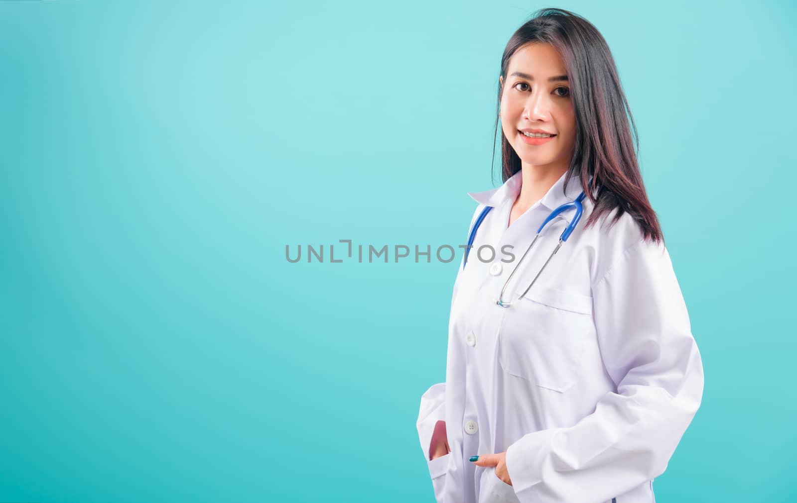 Portrait asian beautiful doctor woman smiling her standing with Hands in Pockets on blue background, with copy space for text