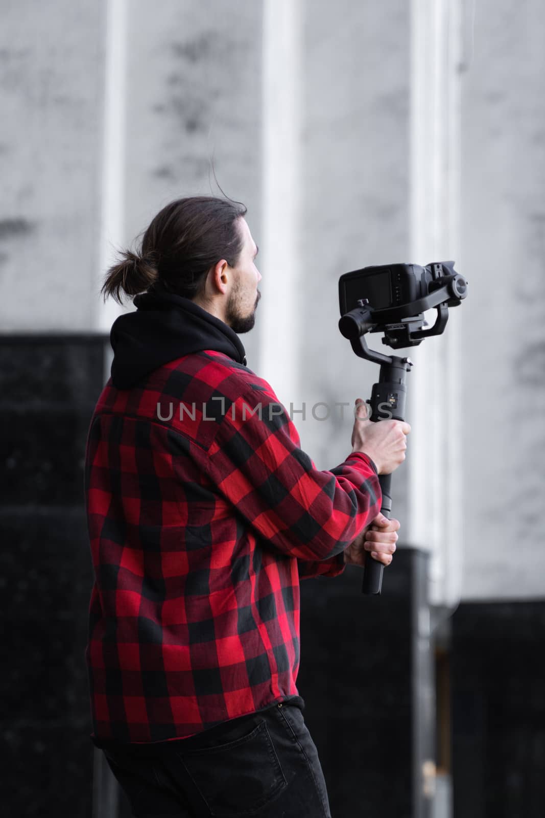 Young Professional videographer holding professional camera on 3-axis gimbal stabilizer. Pro equipment helps to make high quality video without shaking. Cameraman wearing red shirt making a videos