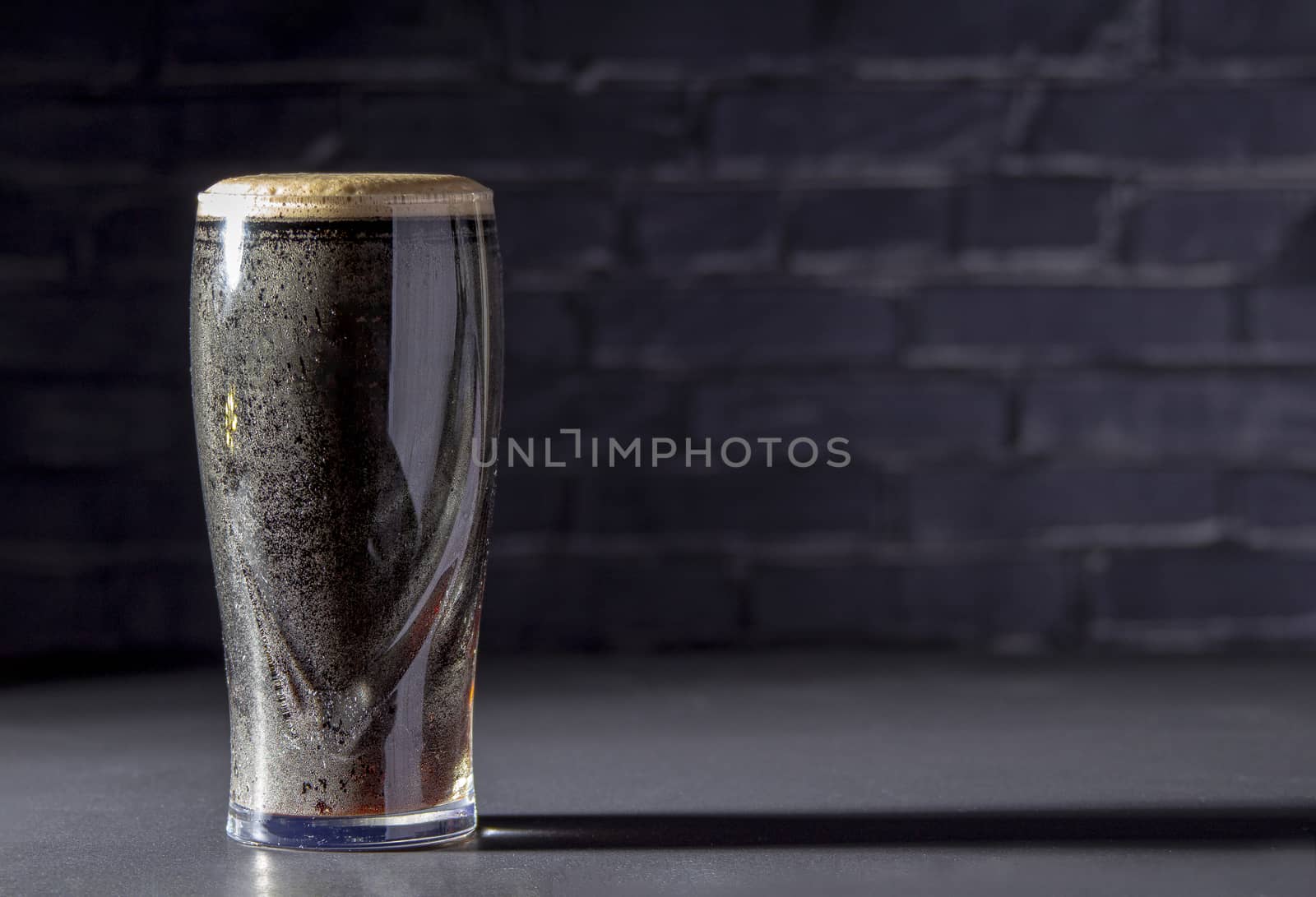 A dark Irish dry stout beer glass with a black brick on the background by oasisamuel