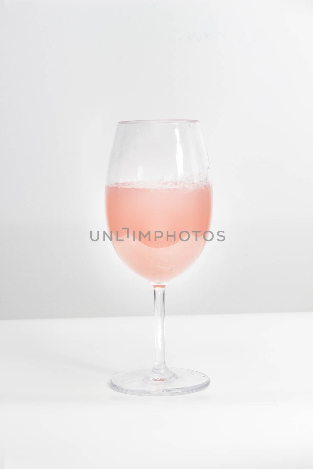 A cup of rose wine on a white table and background by oasisamuel