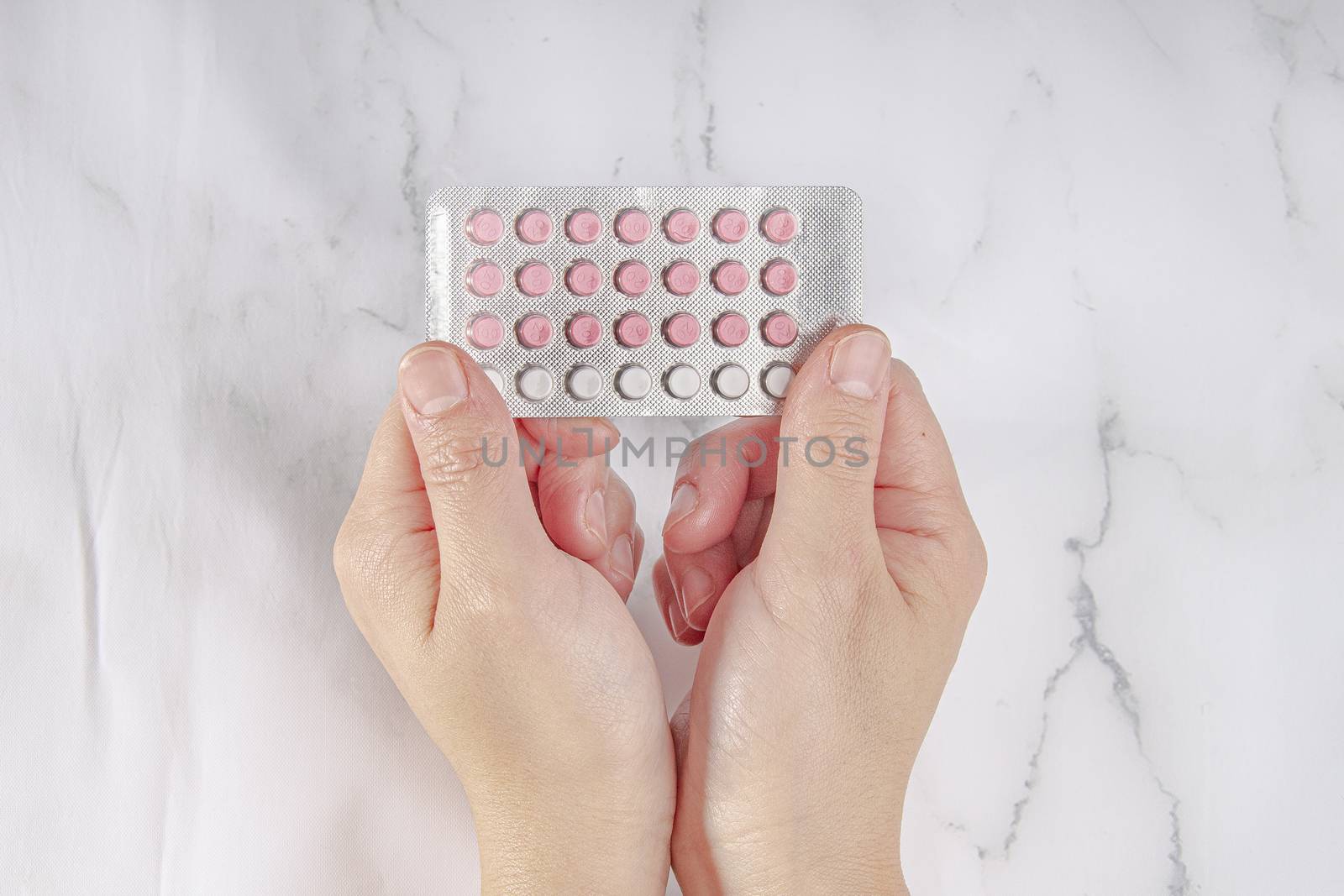 Female hands holding birth control pills on a marble background by oasisamuel