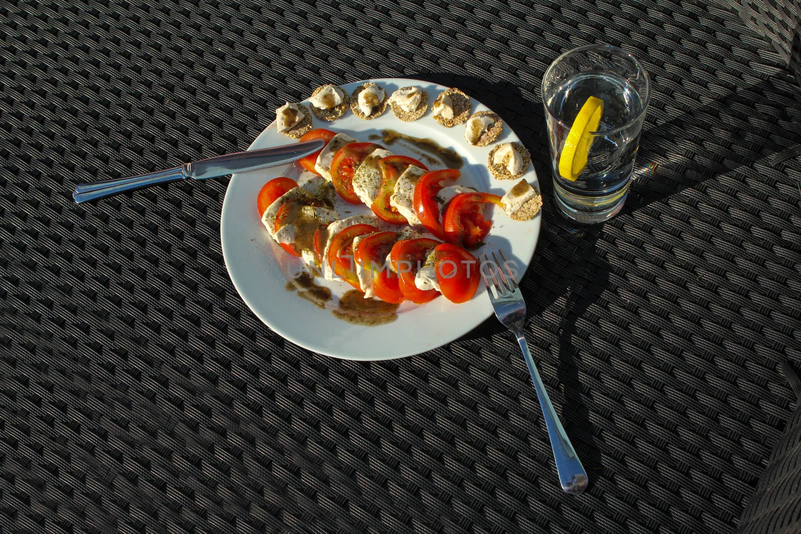 Mozzarella salad with water served outdoors on lounge chair with water and lemon slice