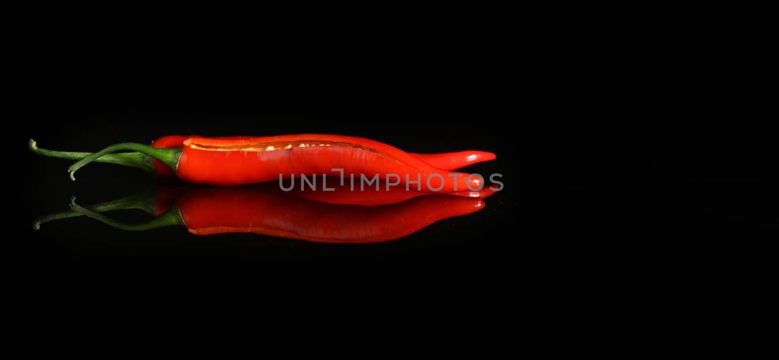 black background with red hot pepper and reflection with copy space