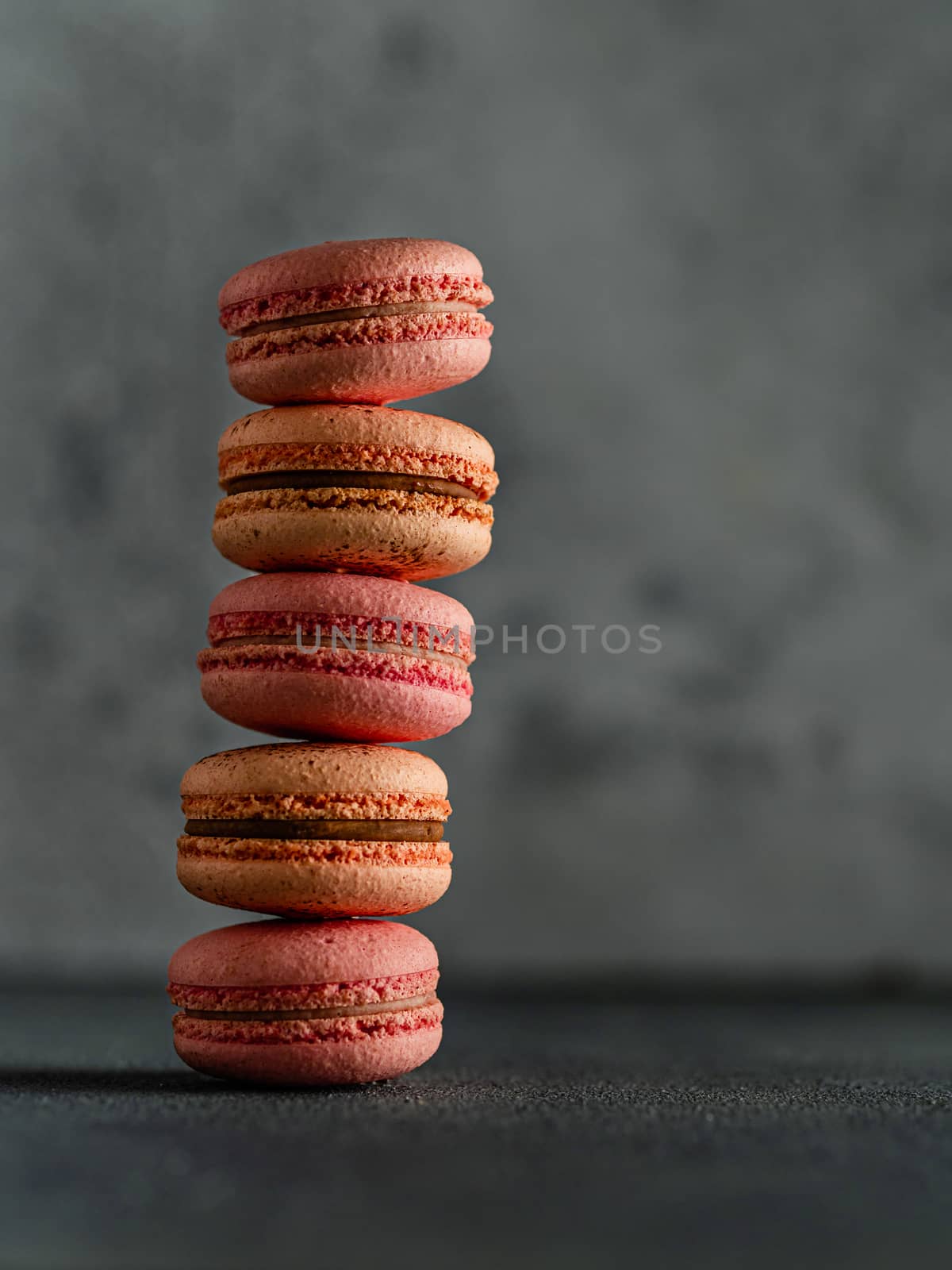 Stack of perfect french macarons. Vertical row of peach and pink macarons on gray textured background, copy space right. Vertical