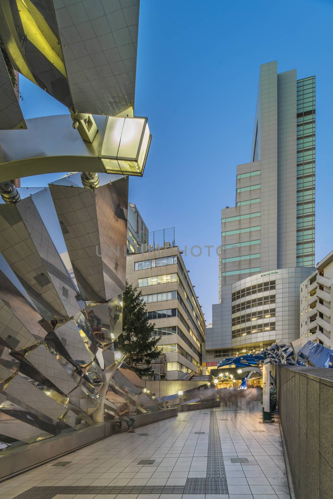 Futuristic architecture with mirroring and transparent blue plastic panels swiveling in Shibuya district in Dogenzaka street leading to Shibuya Crossing Intersection in front of Shibuya Station in a summer evening.