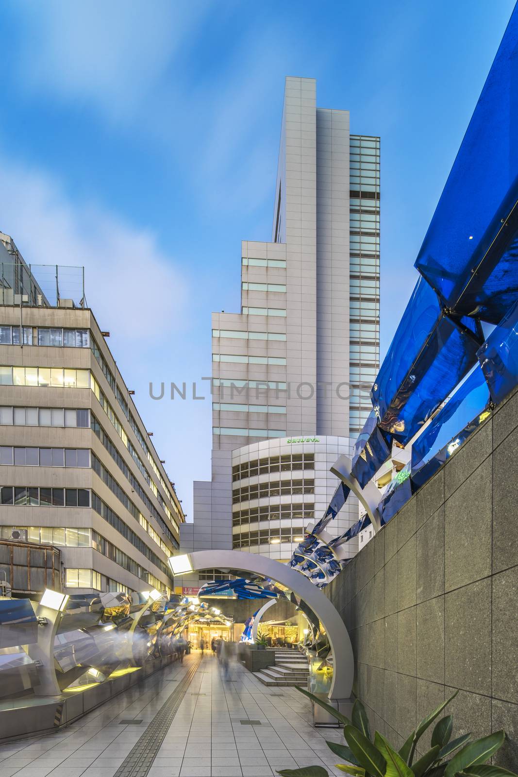 Futuristic architecture with mirroring and transparent blue plastic panels swiveling in Shibuya district in Dogenzaka street leading to Shibuya Crossing Intersection in front of Shibuya Station in a summer evening.