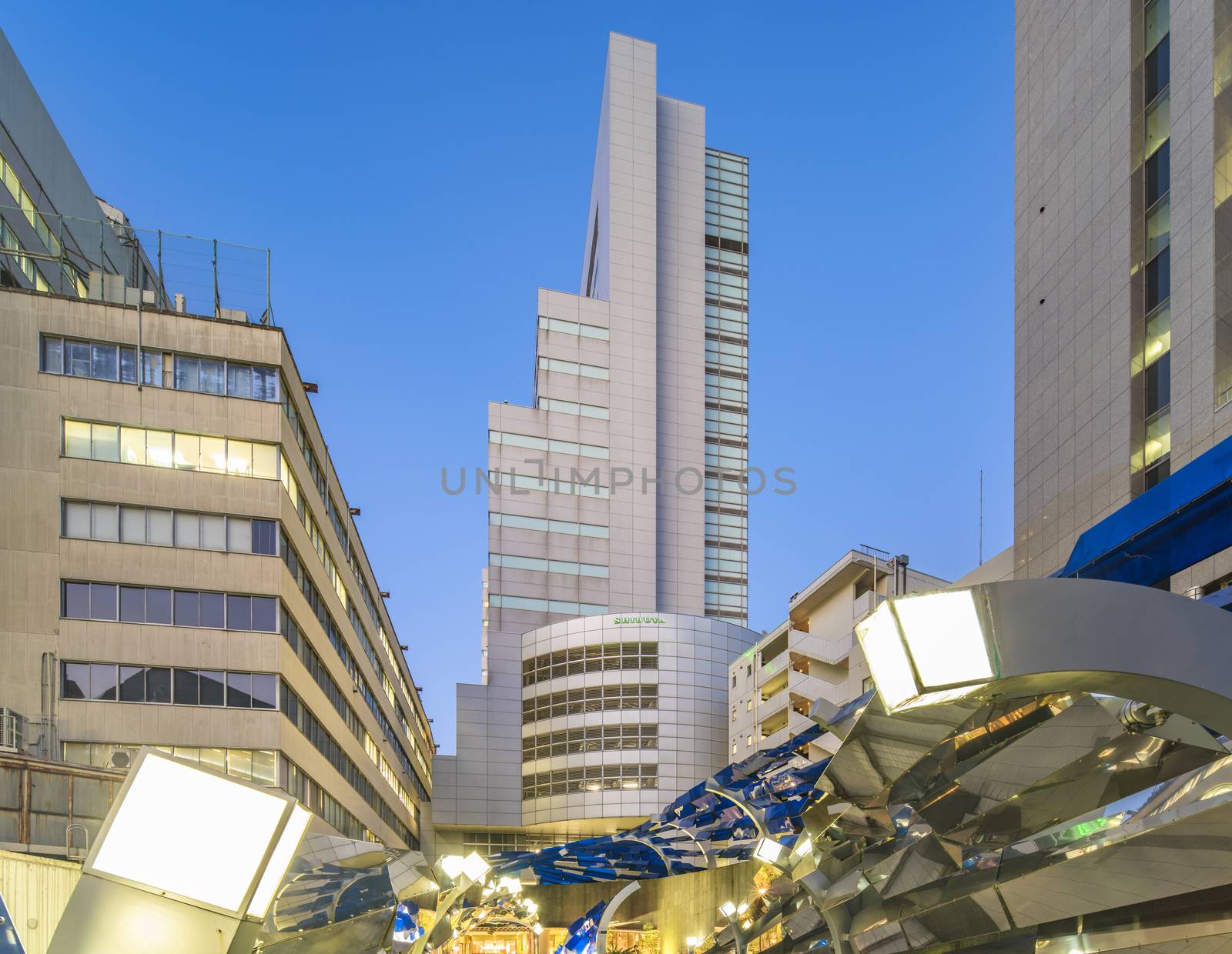 Futuristic architecture with mirroring and transparent blue plastic panels swiveling in Shibuya district in Dogenzaka street leading to Shibuya Crossing Intersection in front of Shibuya Station in a summer evening.