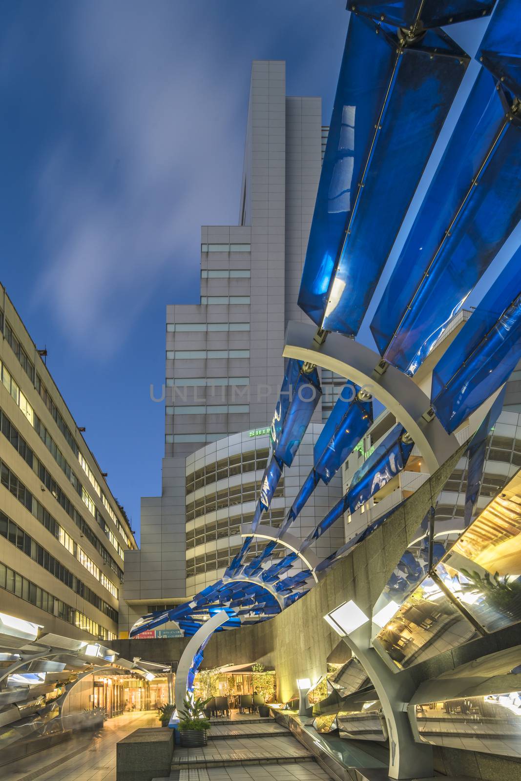 Futuristic architecture with mirroring and transparent blue plastic panels swiveling in Shibuya district in Dogenzaka street leading to Shibuya Crossing Intersection in front of Shibuya Station in a summer evening.