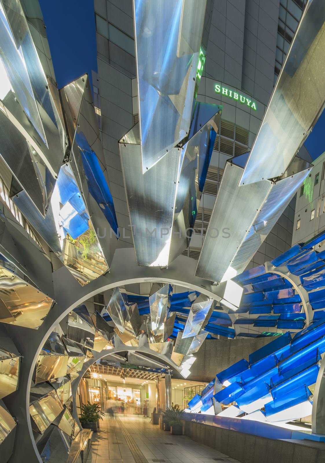 Futuristic architecture with mirroring and transparent blue plastic panels swiveling in Shibuya district in Dogenzaka street leading to Shibuya Crossing Intersection in front of Shibuya Station in a summer evening.