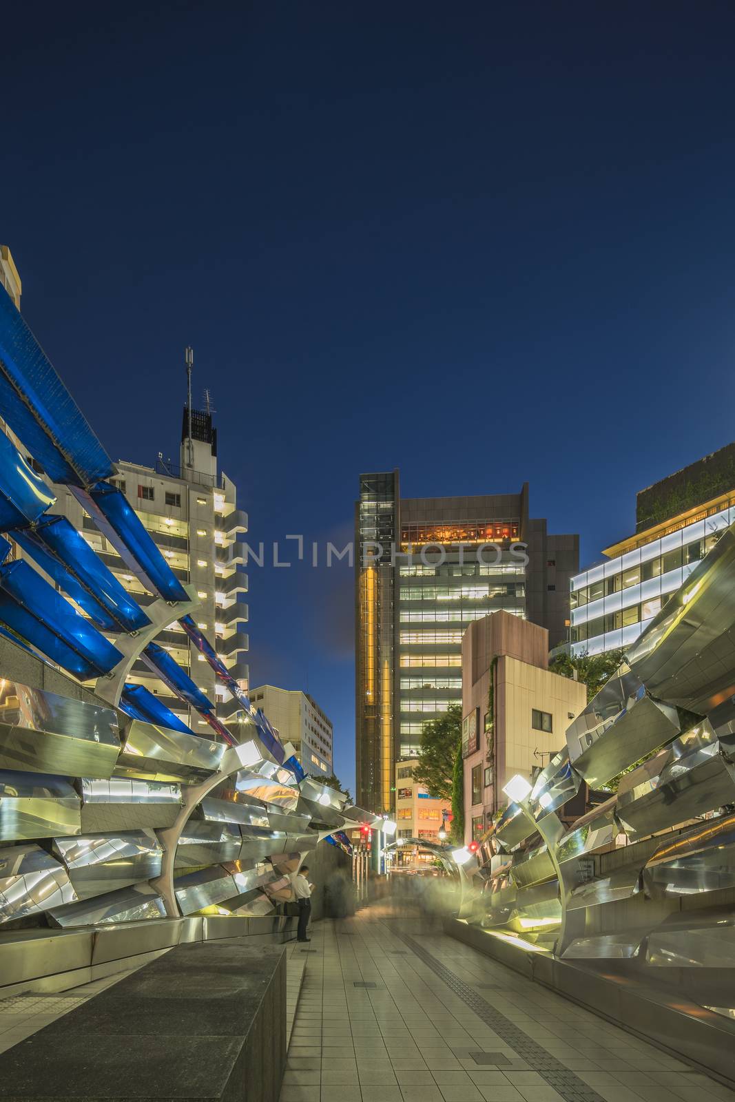 Futuristic architecture with mirroring and transparent blue plastic panels swiveling in Shibuya district in Dogenzaka street leading to Shibuya Crossing Intersection in front of Shibuya Station in a summer evening.