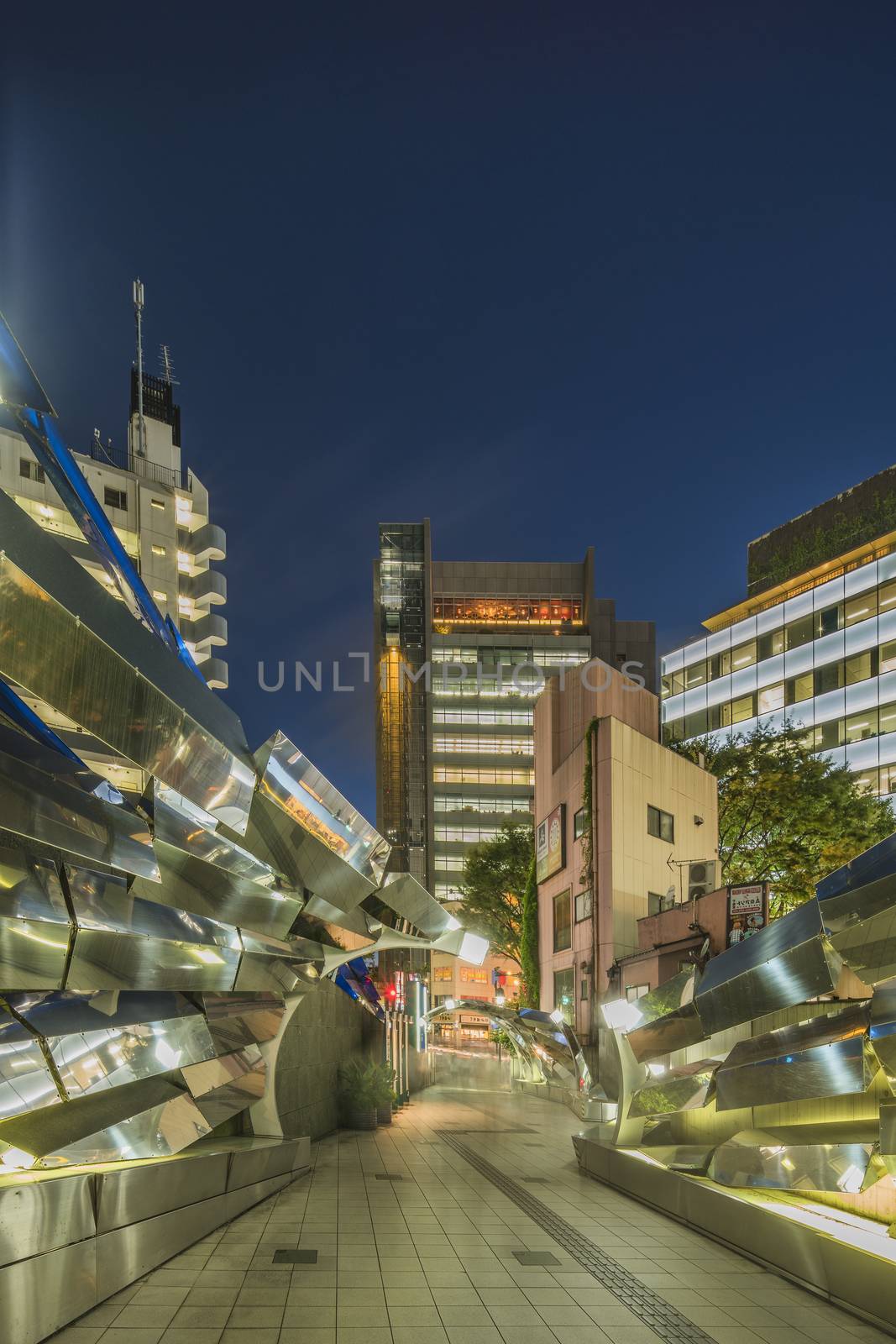 Futuristic architecture with mirroring and transparent blue plastic panels swiveling in Shibuya district in Dogenzaka street leading to Shibuya Crossing Intersection in front of Shibuya Station in a summer evening.