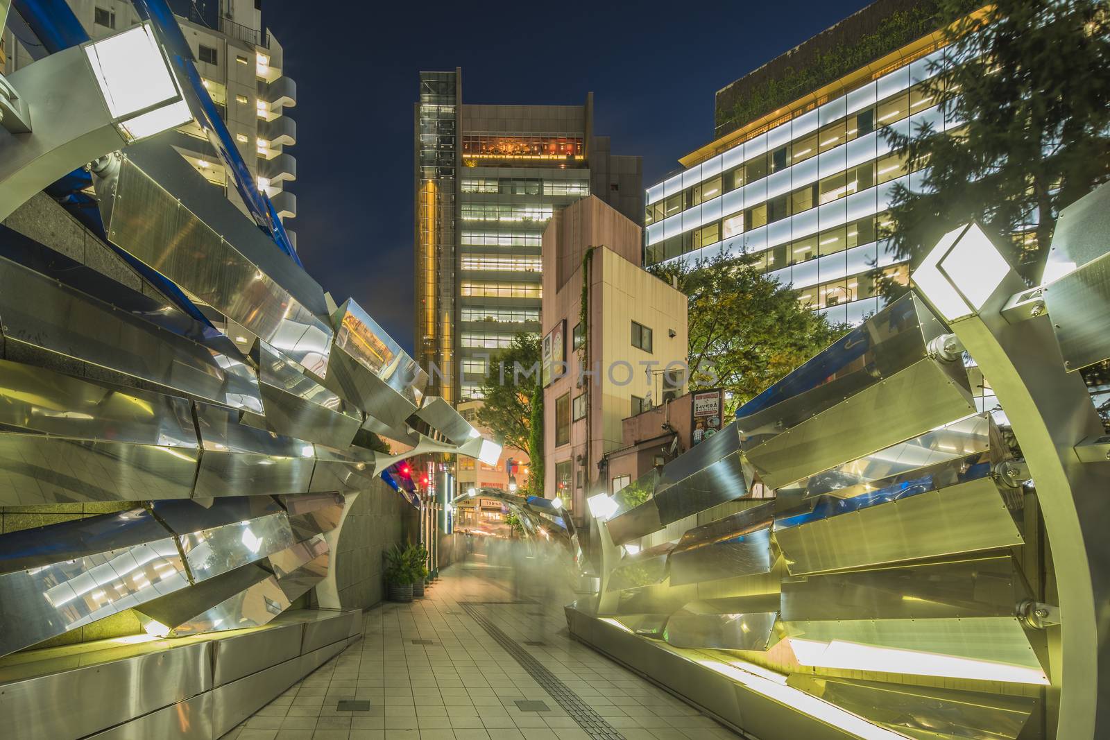Futuristic architecture with mirroring and transparent blue plastic panels swiveling in Shibuya district in Dogenzaka street leading to Shibuya Crossing Intersection in front of Shibuya Station in a summer evening.