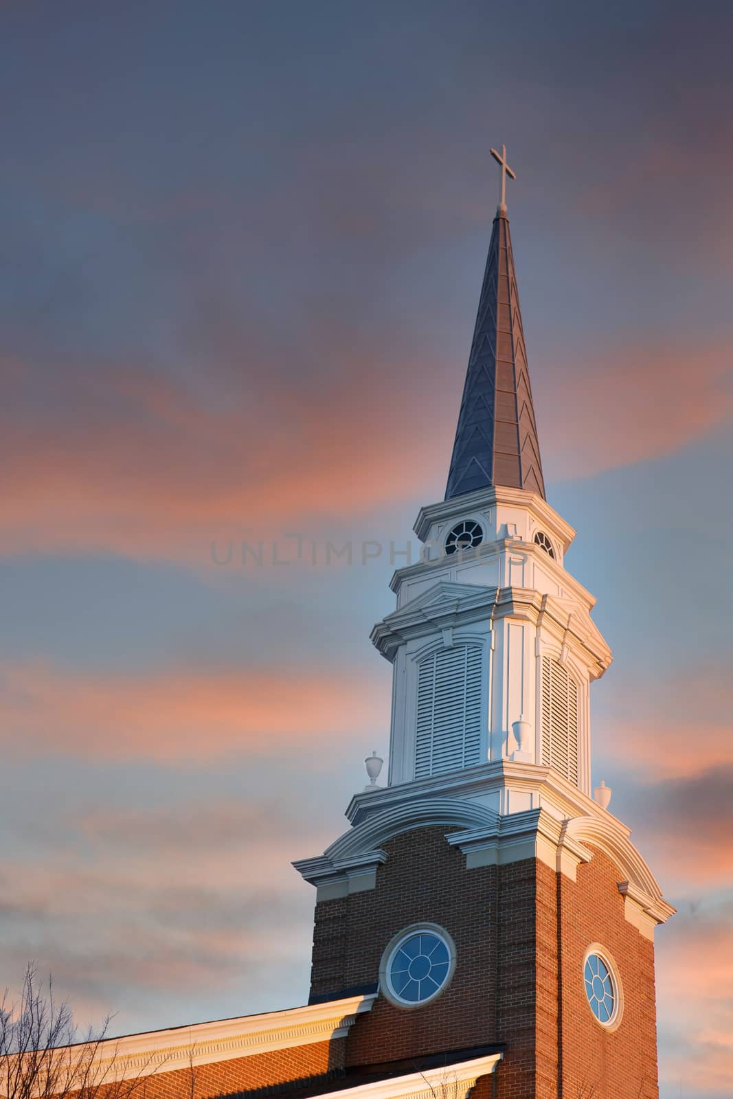 A baptist church steeple rising into a clear blue early morning sky with half moon in background