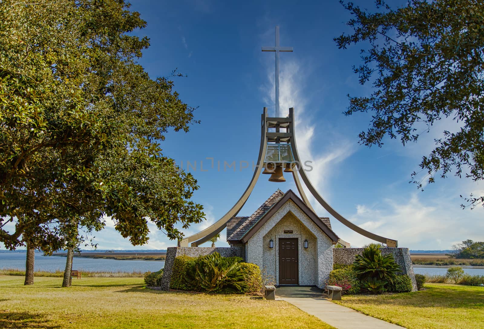 A small building housing church bells under a cross in a park by a wetland marsh