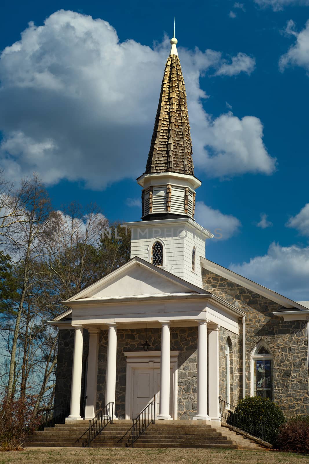 An old wood and stone church with a wood shingled steeple under clear blue skies