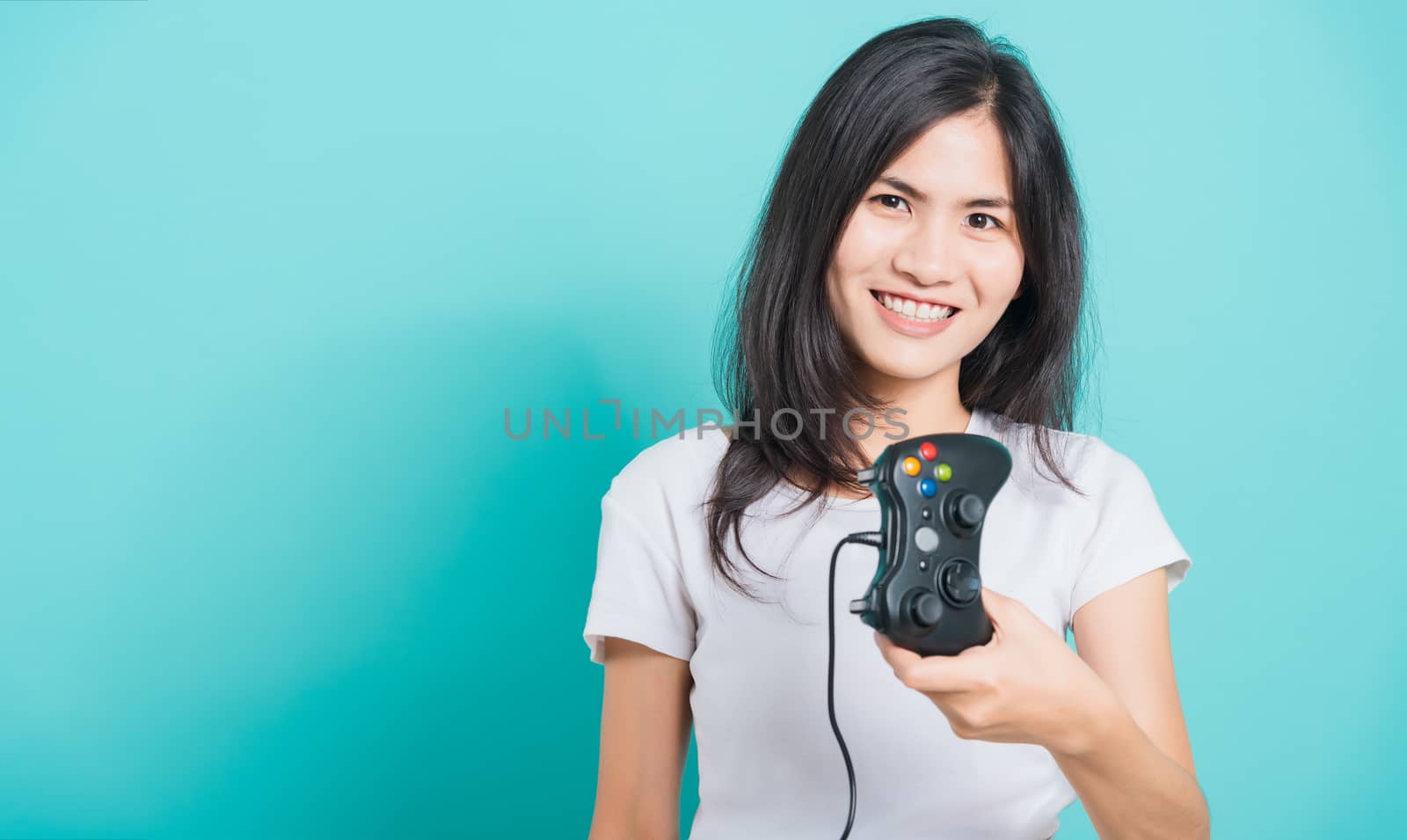 Portrait Asian beautiful happy young woman wear t-shirt gamer with a joystick or gamepad in hands, on blue background, with copy space
