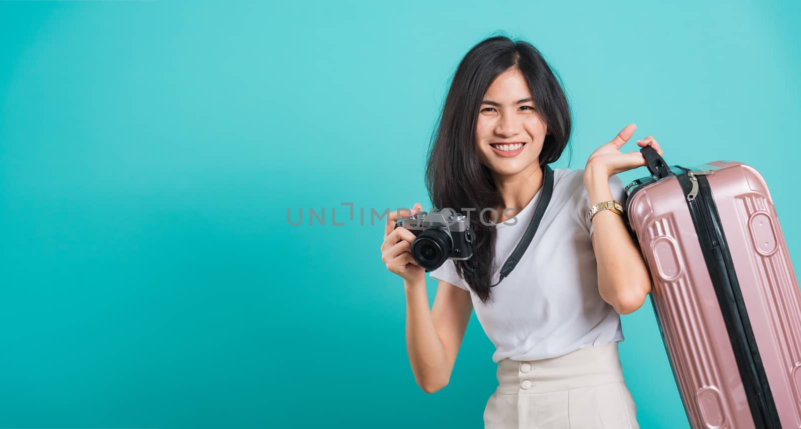 Traveler tourist happy Asian beautiful young woman standing wear white t-shirt, holidays travel concept, her holding suitcase bag and photo mirrorless camera, shoot photo in studio on blue background