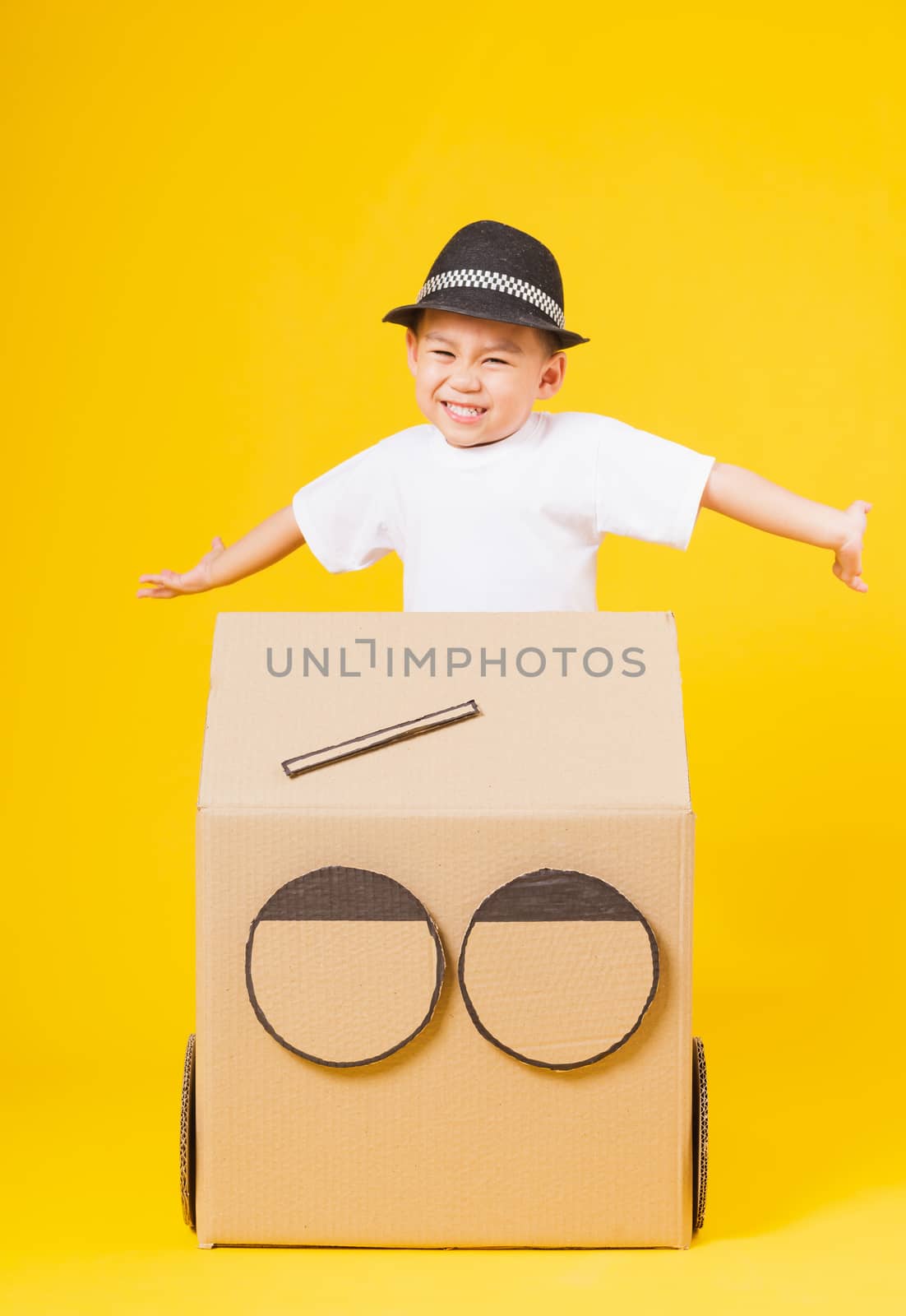 Portrait happy Asian cute little children boy smile so happy wearing white T-shirt driving car creative by cardboard, studio shot on yellow background with copy space