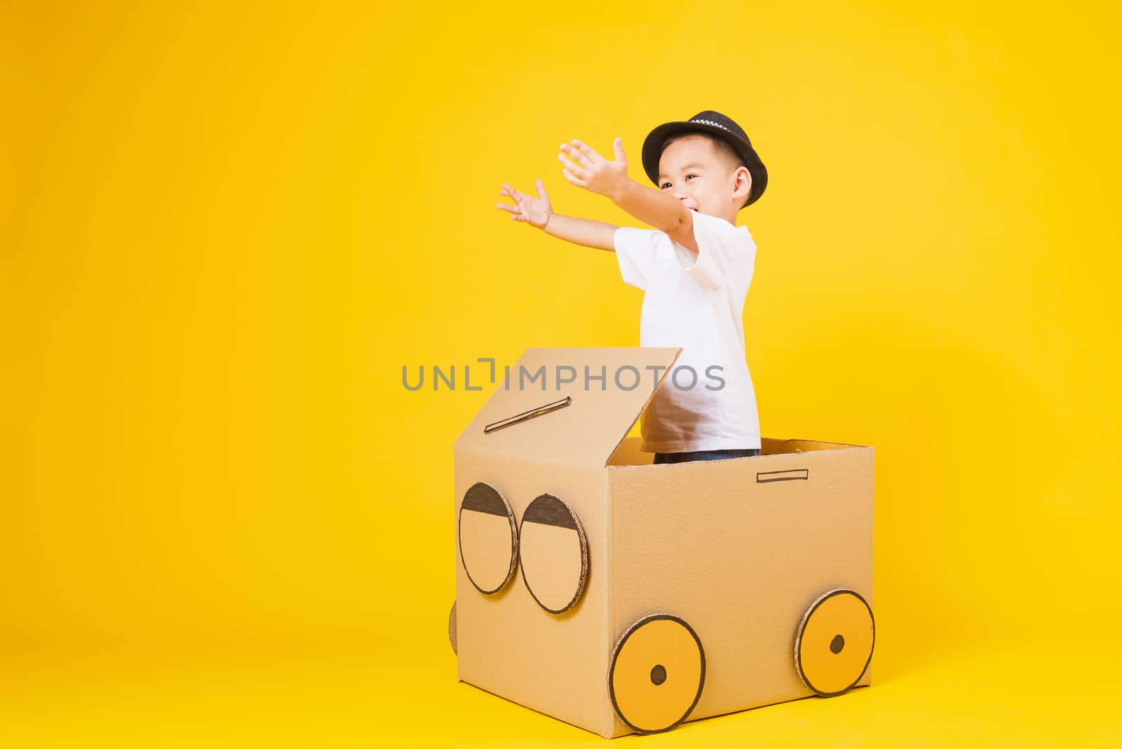 Portrait happy Asian cute little children boy smile so happy wearing white T-shirt driving car creative by cardboard, studio shot on yellow background with copy space